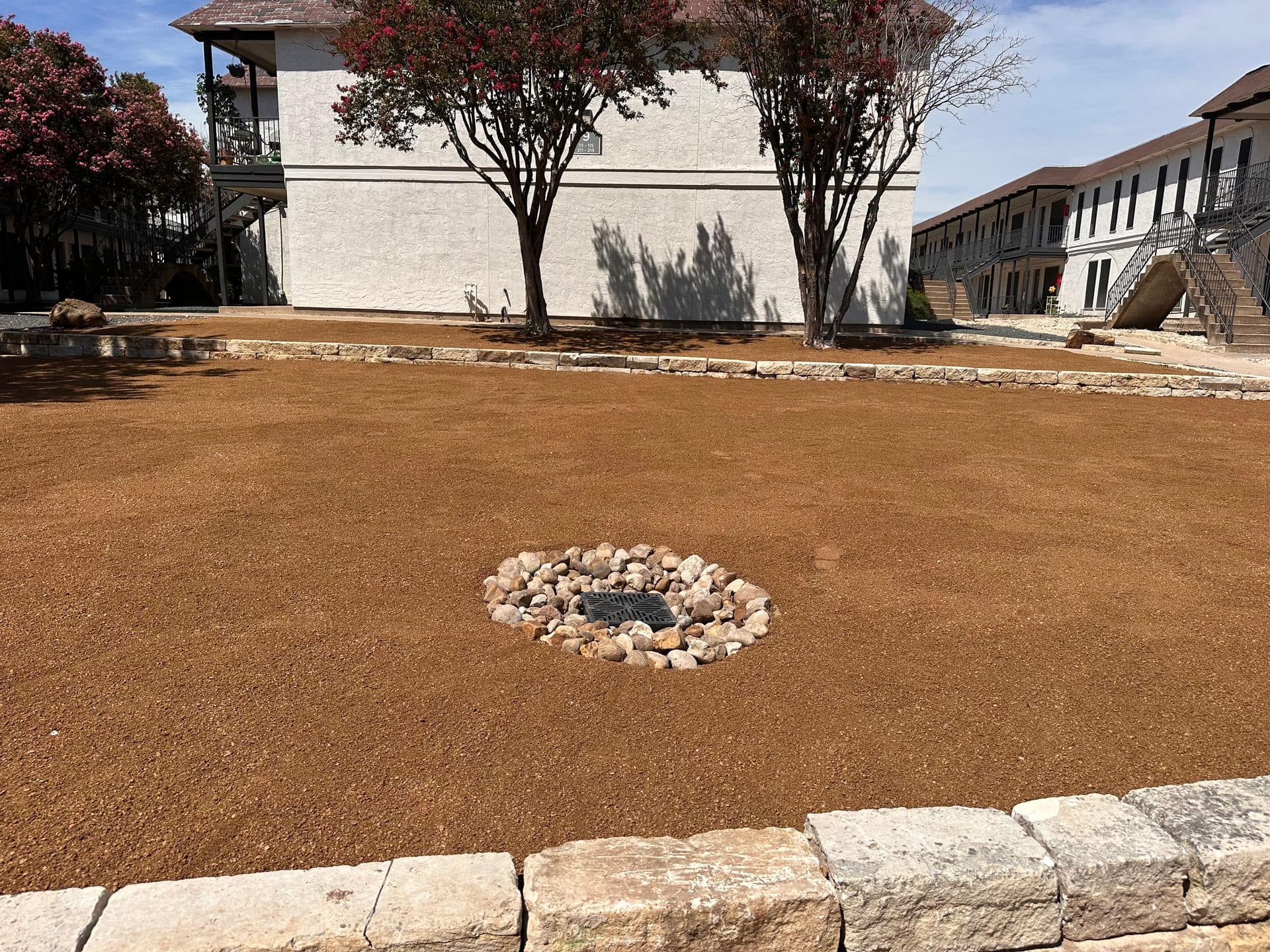 Gravel yard with stone fire pit and drainage-friendly landscaping in Austin, TX, showing proper soil drainage design