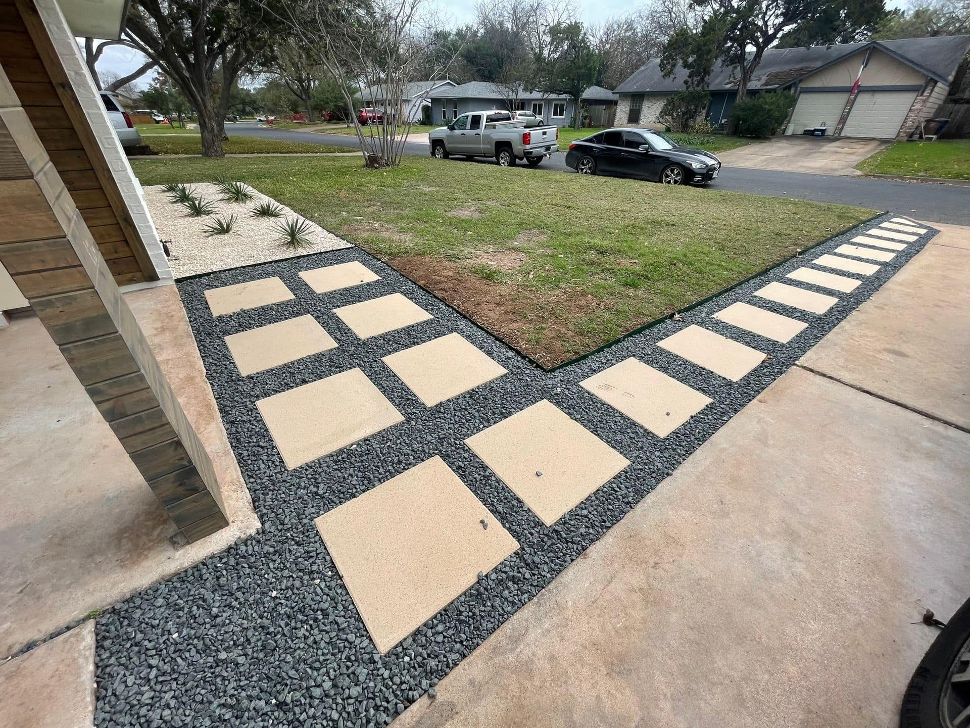 Shows concrete pavers integrated with a dark decorative gravel border along a driveway/walkway.
