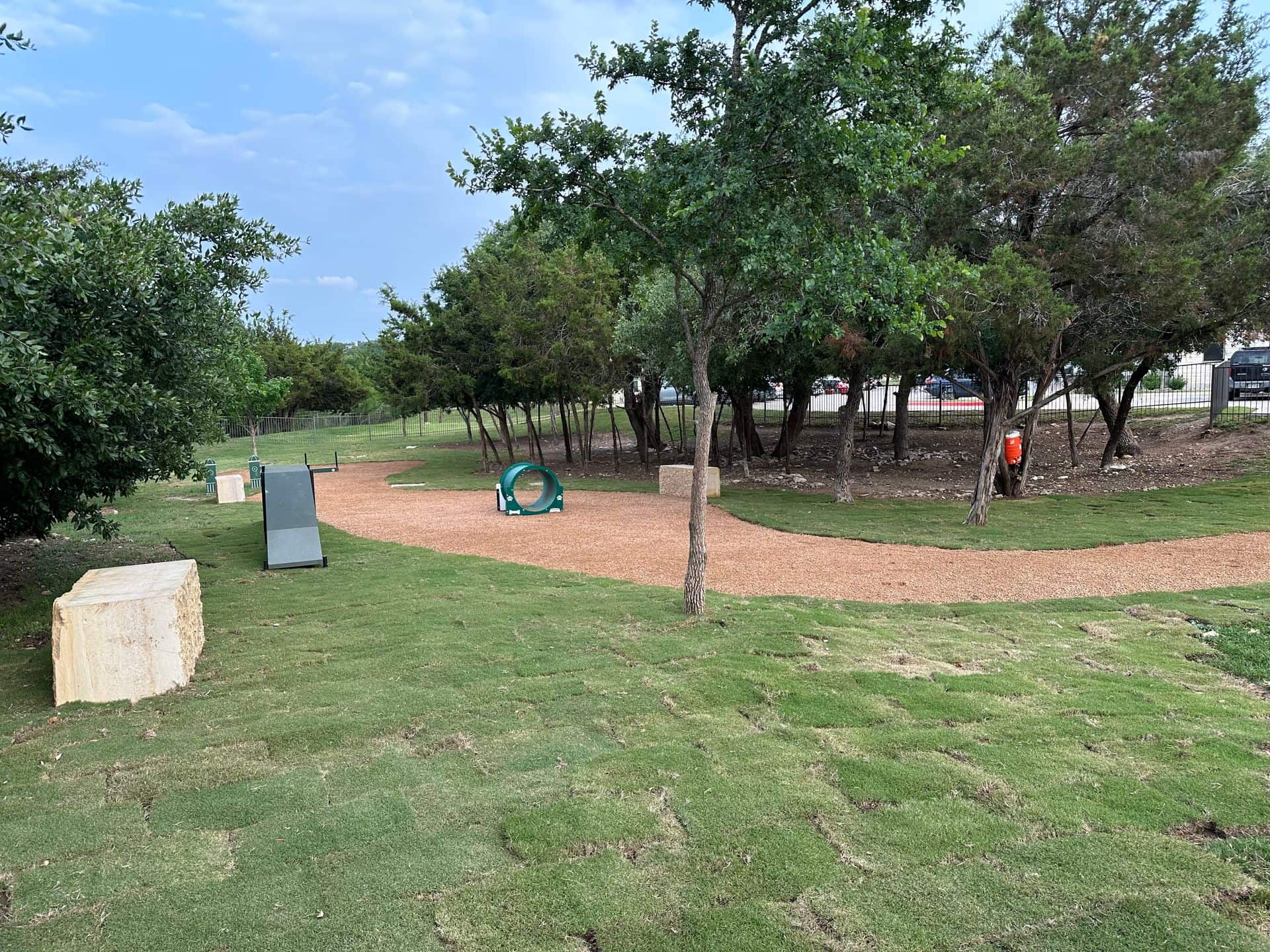 Dog park with walking path, agility equipment, trees, and grassy areas.