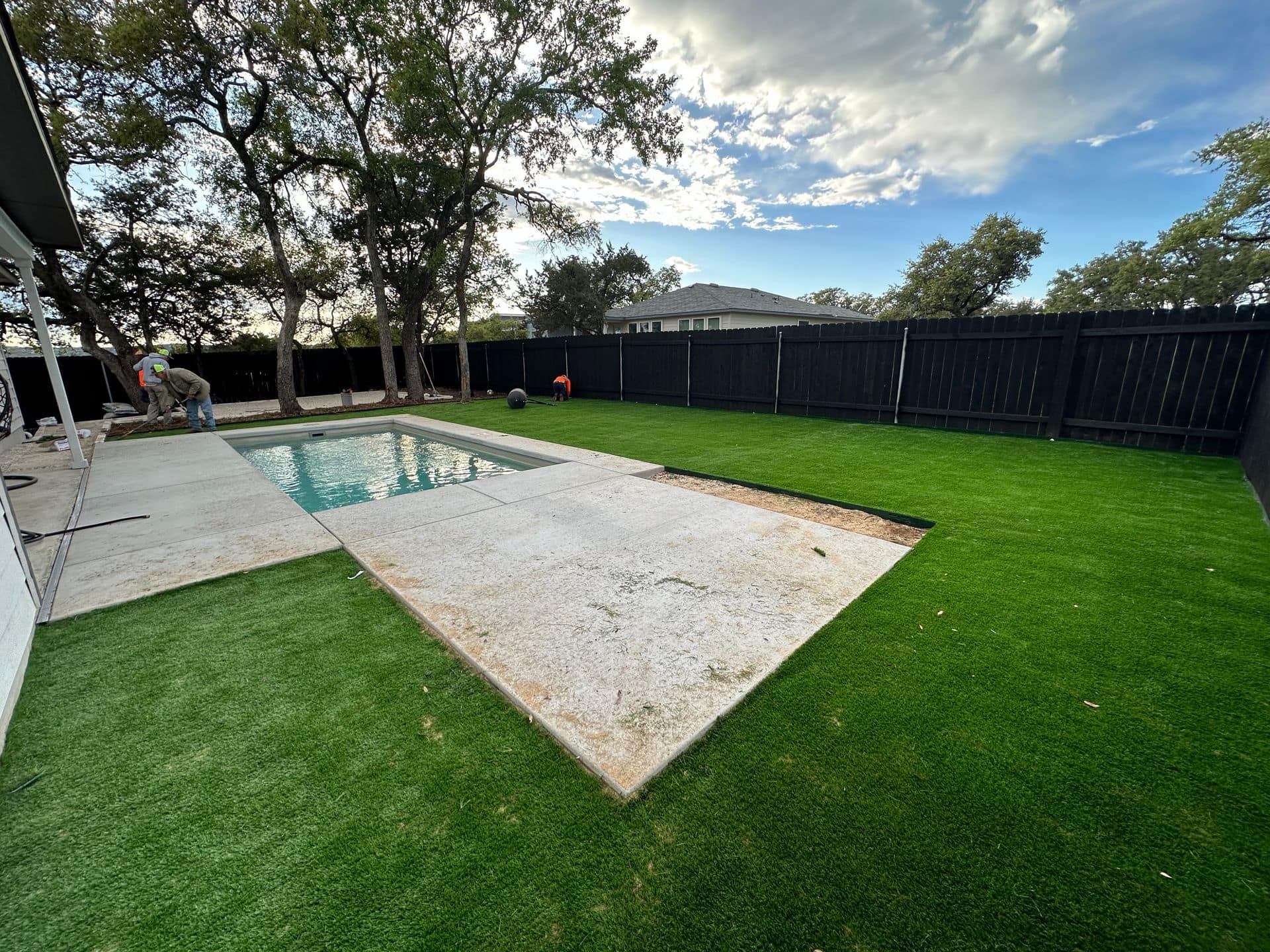 A 7 Kings Landscaping crew finishing a full backyard project in Austin with new turf, a poured concrete patio and a pool set under mature live oaks.