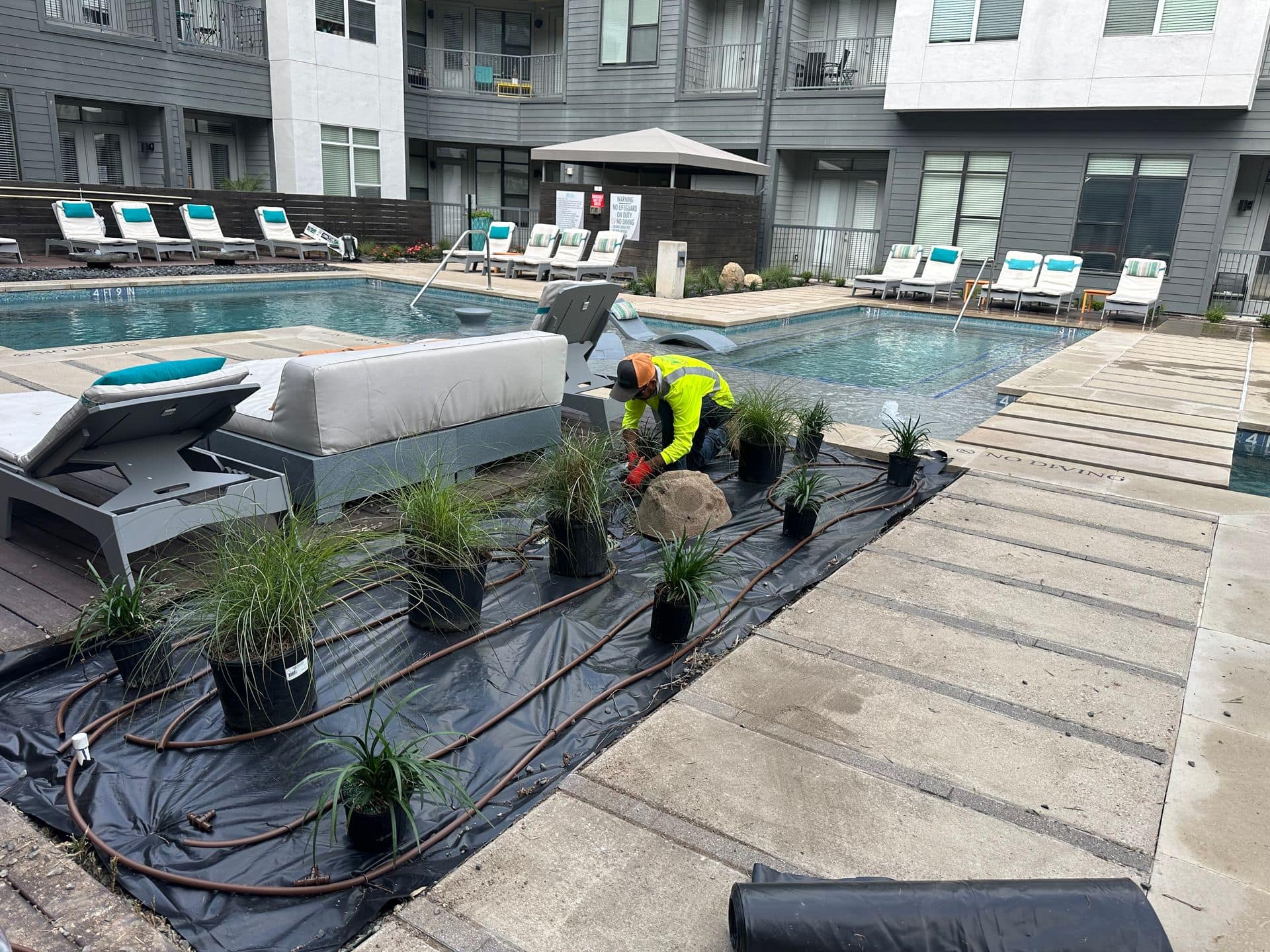 A 7 Kings Landscaping crew member installing irrigation line and drip tubing through a new planting bed beside the pool deck at an Austin apartment property.