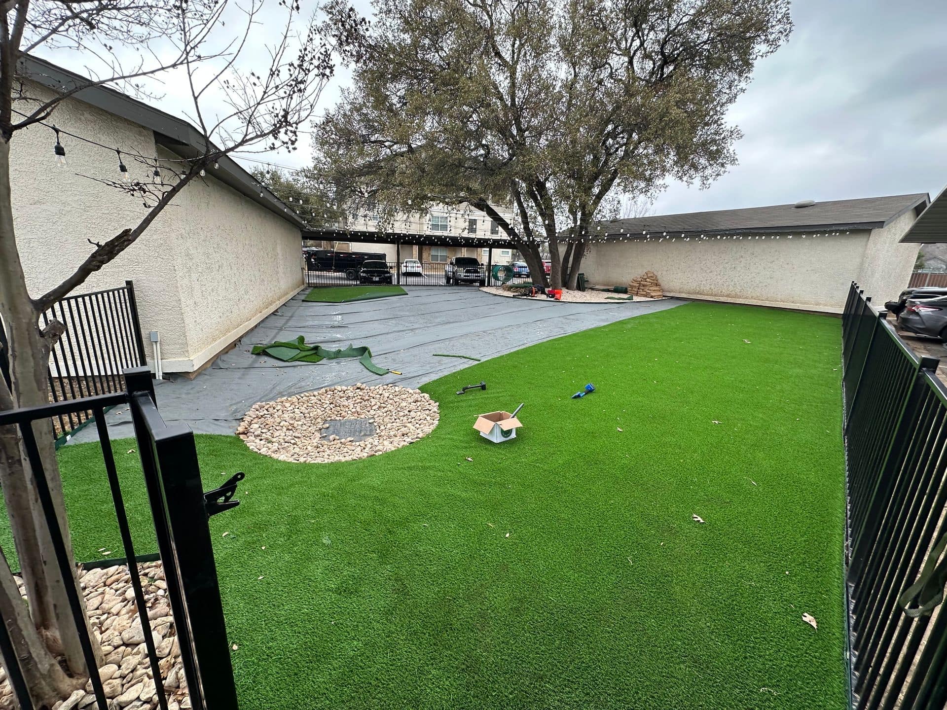 Small fenced backyard with green turf, a rock drain, and patio area beside a house.